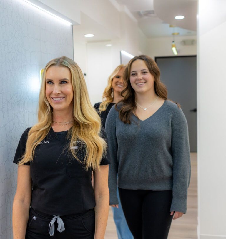 madison-park-family-dentistry-about-our-philosophy-section1 Team member from Madison Park Family Dentistry guiding two smiling patients down a hallway